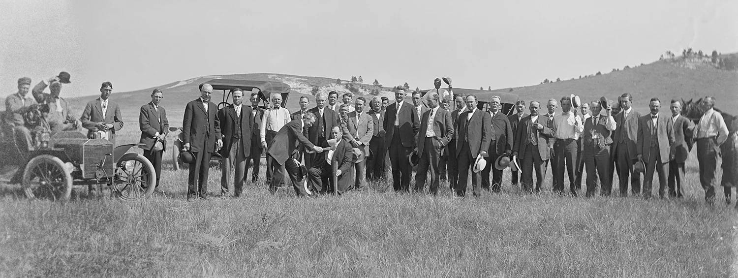 Group of people lined up watching a person hammer a stake in the ground