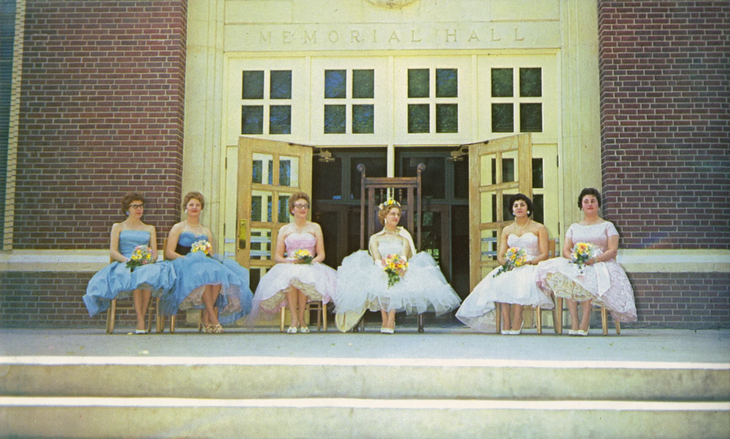 Four students wearing formal gowns in front of an academic building
