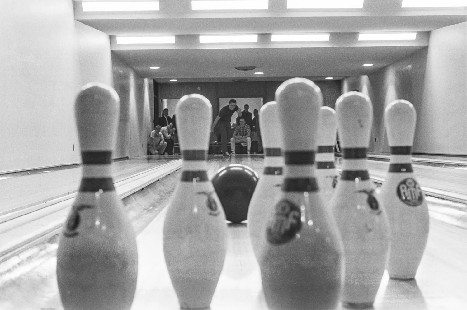 View from behind bowling pins with a ball rolling in and a bowler in the background