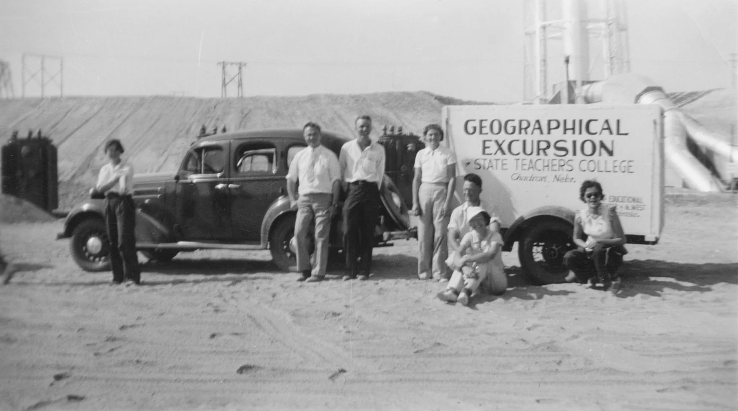Group of people standing in front of a car with towed trailer