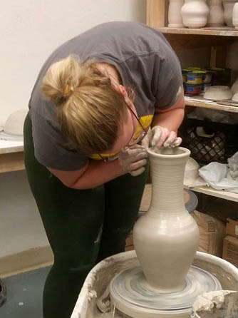 A student works on a thrown piece of artwork
