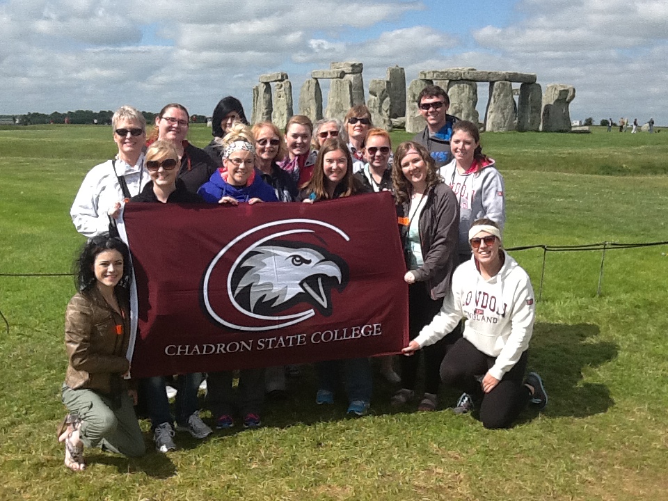 Students on a Study Abroad trip hold a flag in front of Stonehenge