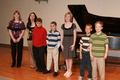 Children musicians pose in front of a piano