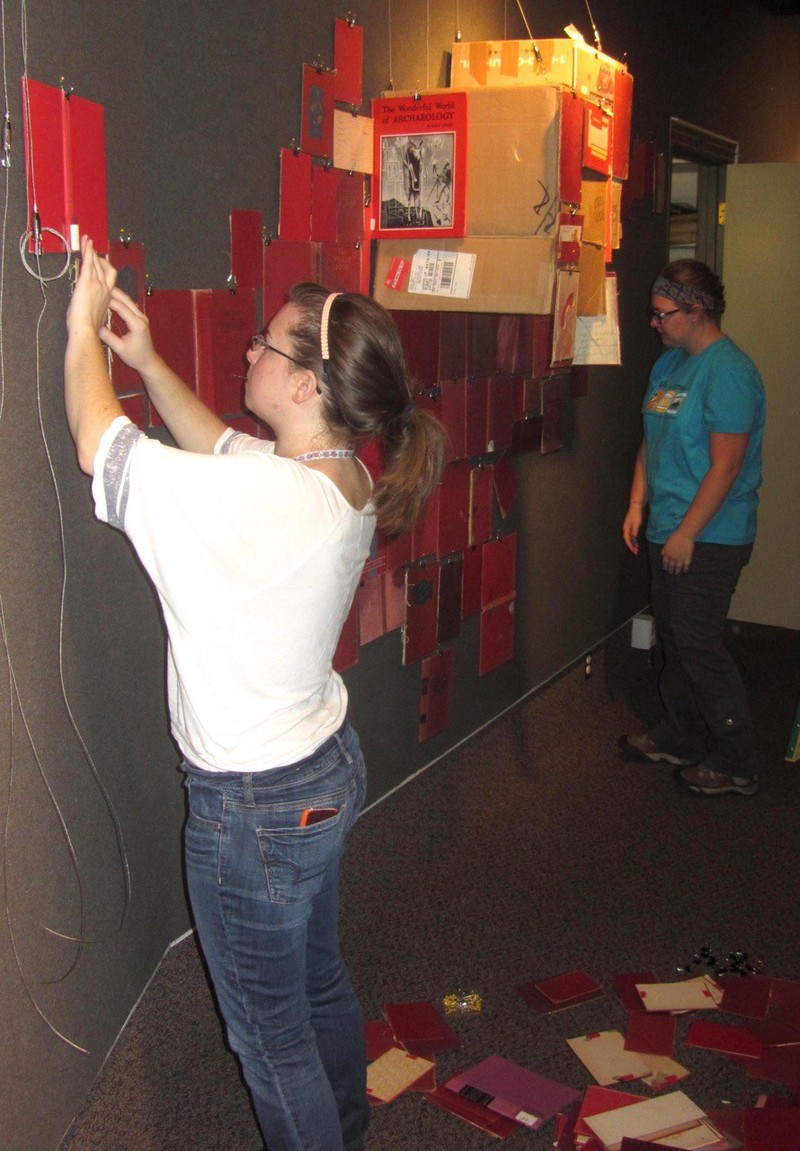 Chadron State College student Mackenzie Carroll and Jessamyn Kostman help artist Todd Christensen