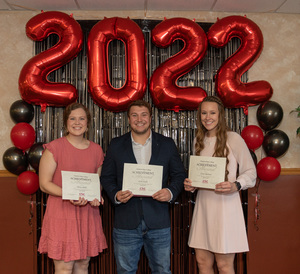 Three health professions students stand holding their awards in front of a 2022 backdrop.