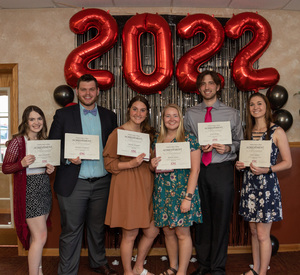 Six students stand with their awards in front of 2022 backdrop.