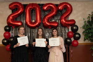 Three students stand holding their awards in front of a 2022 backdrop.