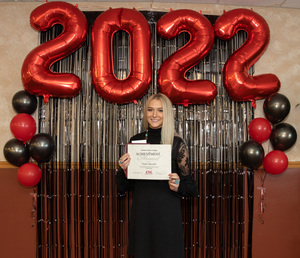 Taylor Buescher stands holding her award in front of a 2022 backdrop.
