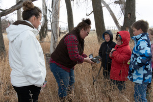 Five people examine a trail camera in a forest