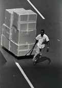 Black and white photo of a worker pulling a cart of cardboard boxes