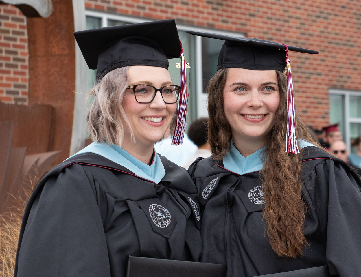 Two graduates posing outside in regalia