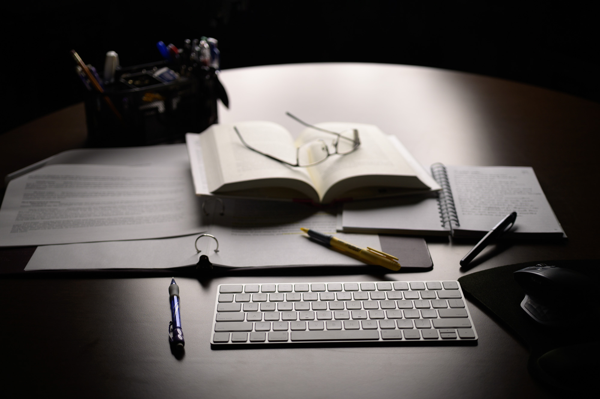 Desk with book, pens, glasses, keyboard, and planners