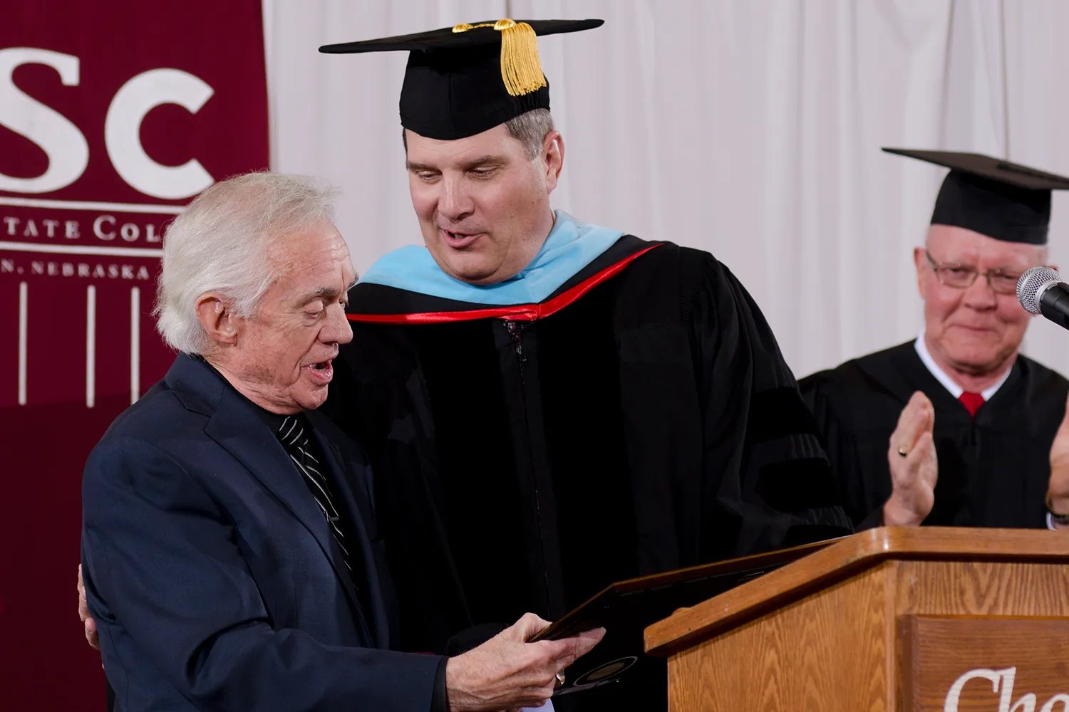 Randy Rhine, Chadron State College interim president, presents the Honorary Doctor of Humane Letters degree to Ron Hull of Lincoln, at left. Giving applause is Gary Bieganski