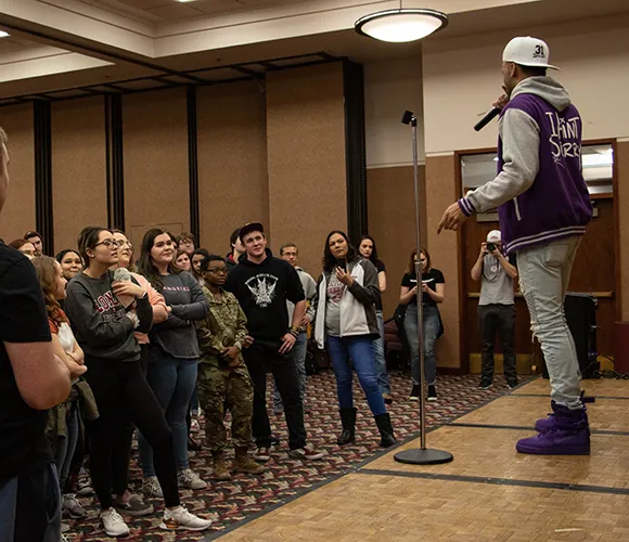 People listening to a presenter standing on a stage speaking into a microphone
