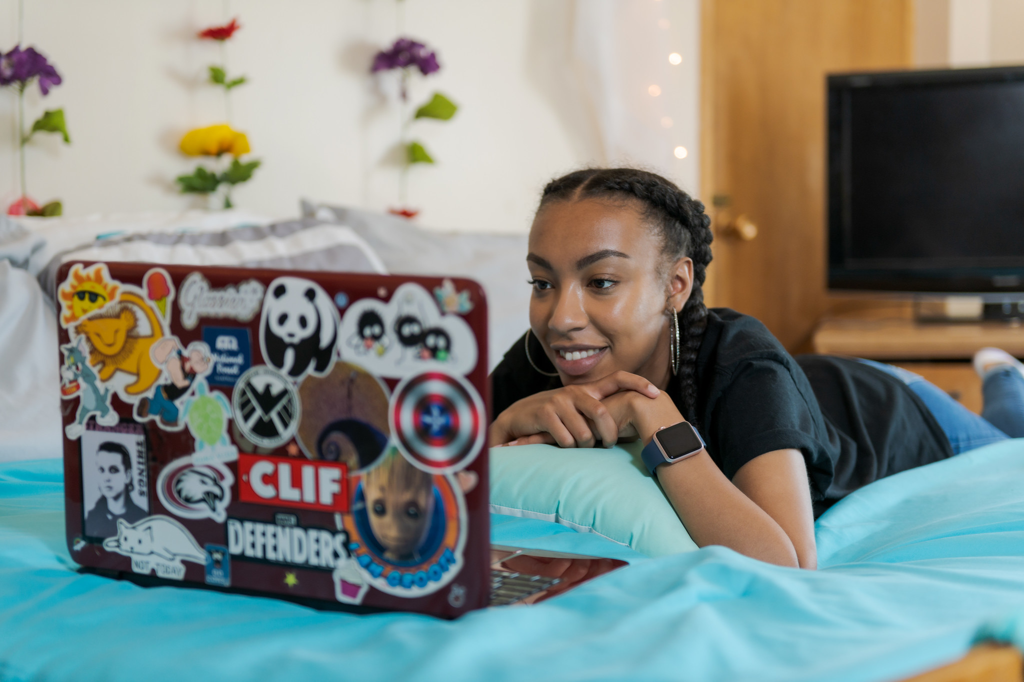 Student happily working on laptop in bedroom. Laptop is covered in stickers.