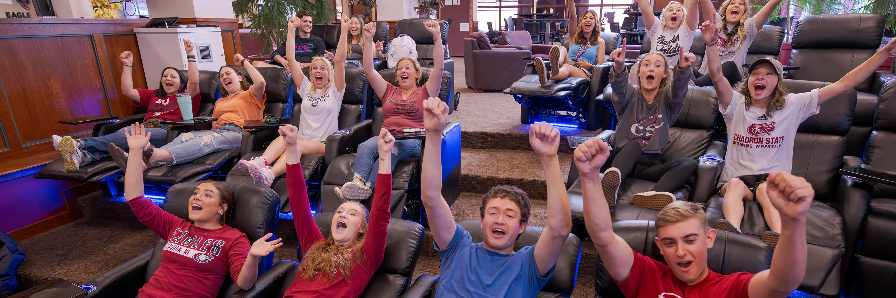 A group of students cheers while watching a game on TV